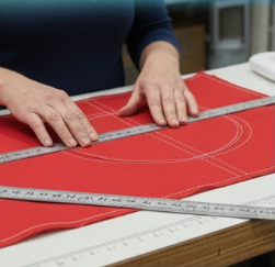 Person measuring red fabric with a ruler on a cutting mat